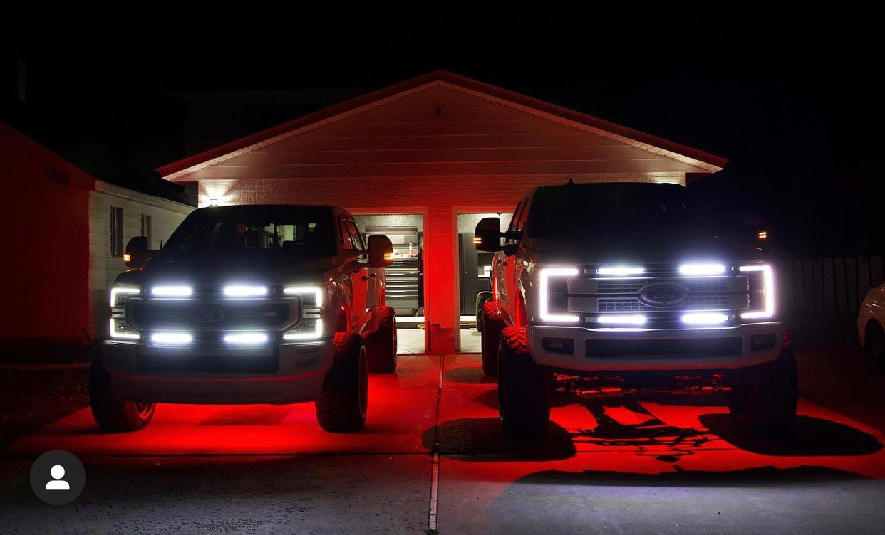 two lifted ford superduty trucks with 4 bar grill lights facing camera